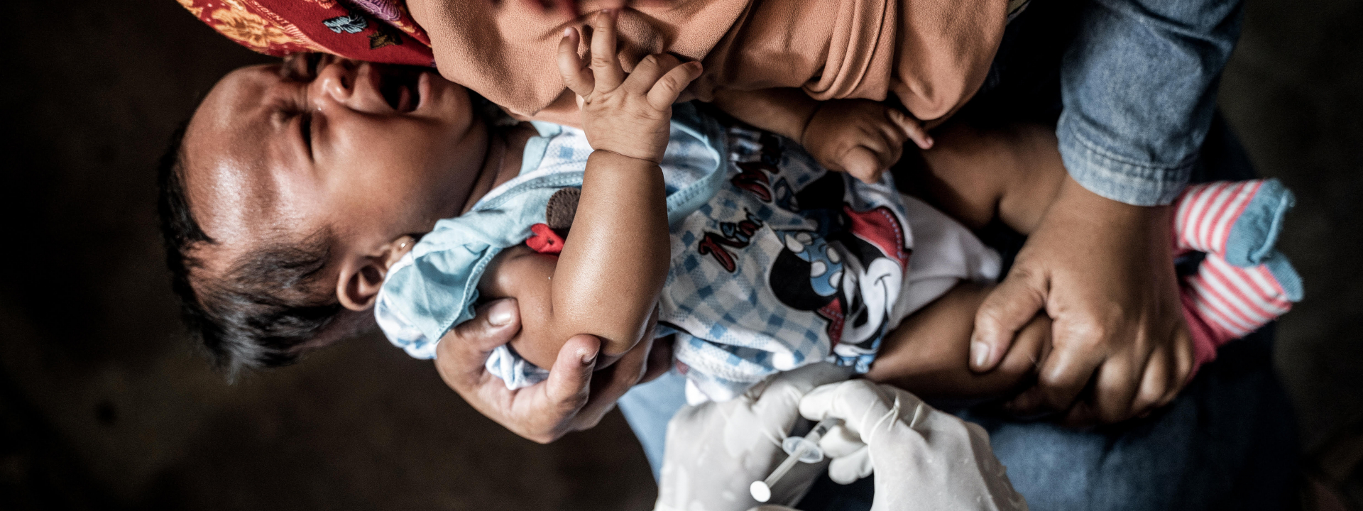 Baby receiving needle injection from doctor in blue hazmat suit