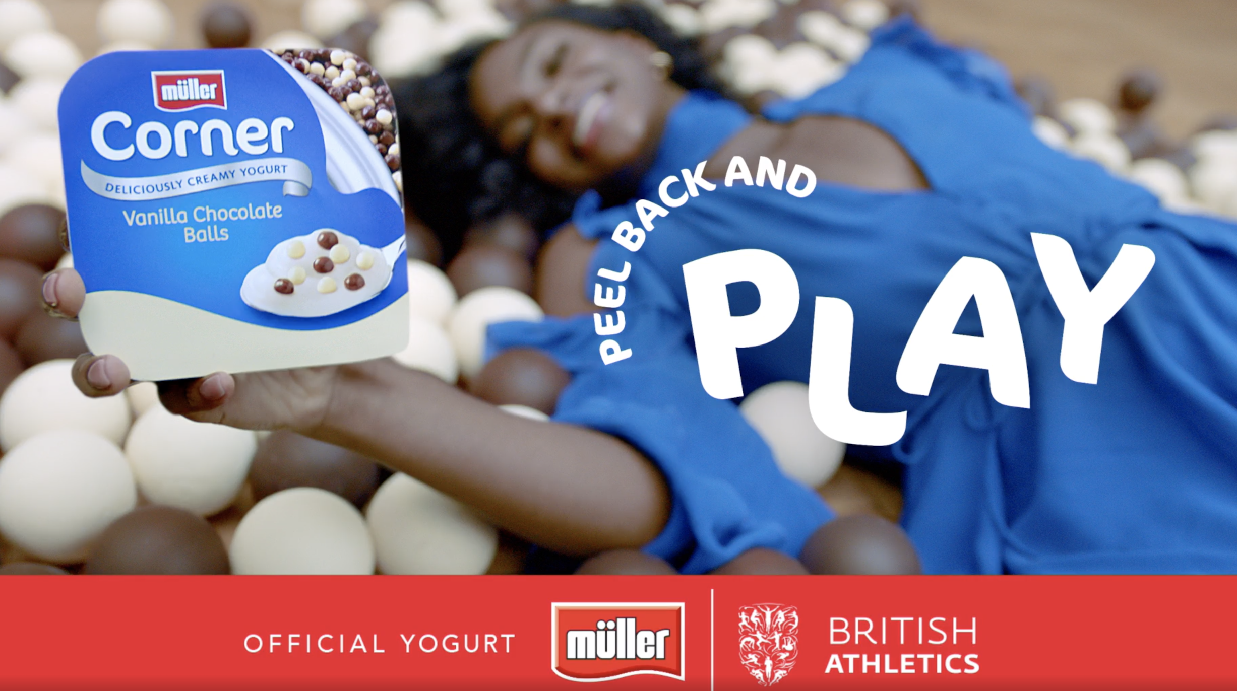 An out of focus woman in a blue dress holding a Muller Corner yogurt to the screen