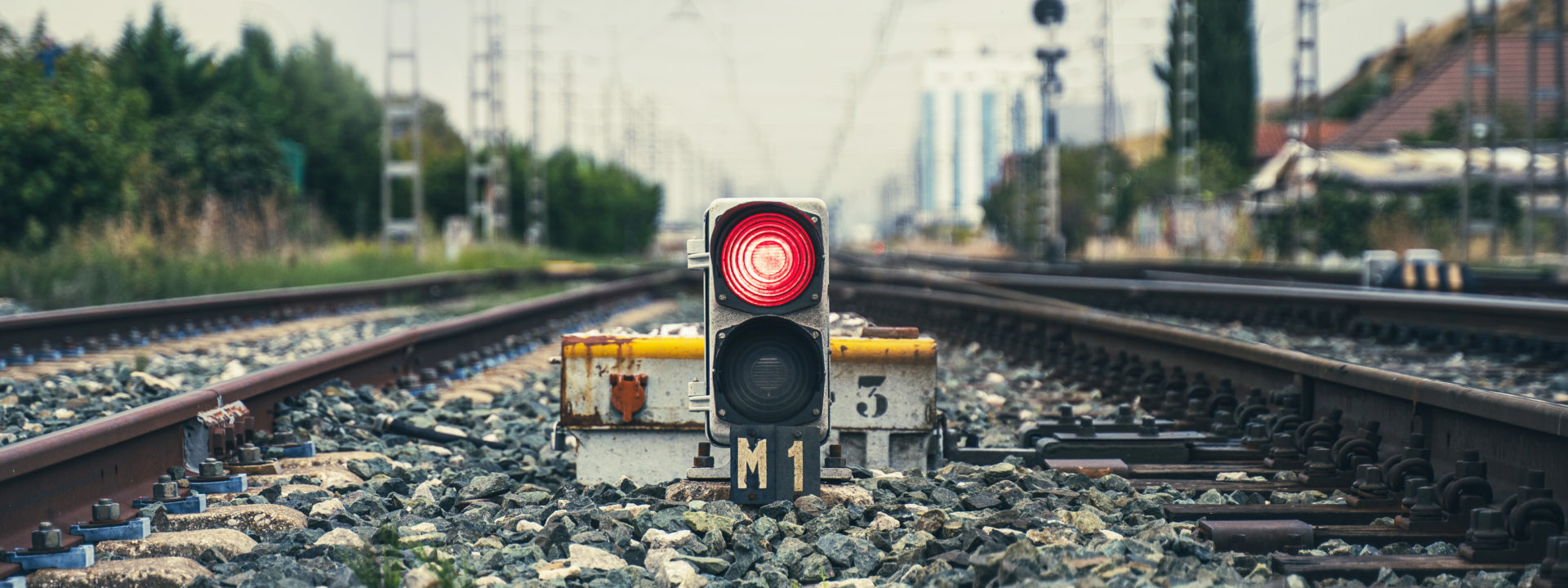 A red traffic light in the middle of some train tracks