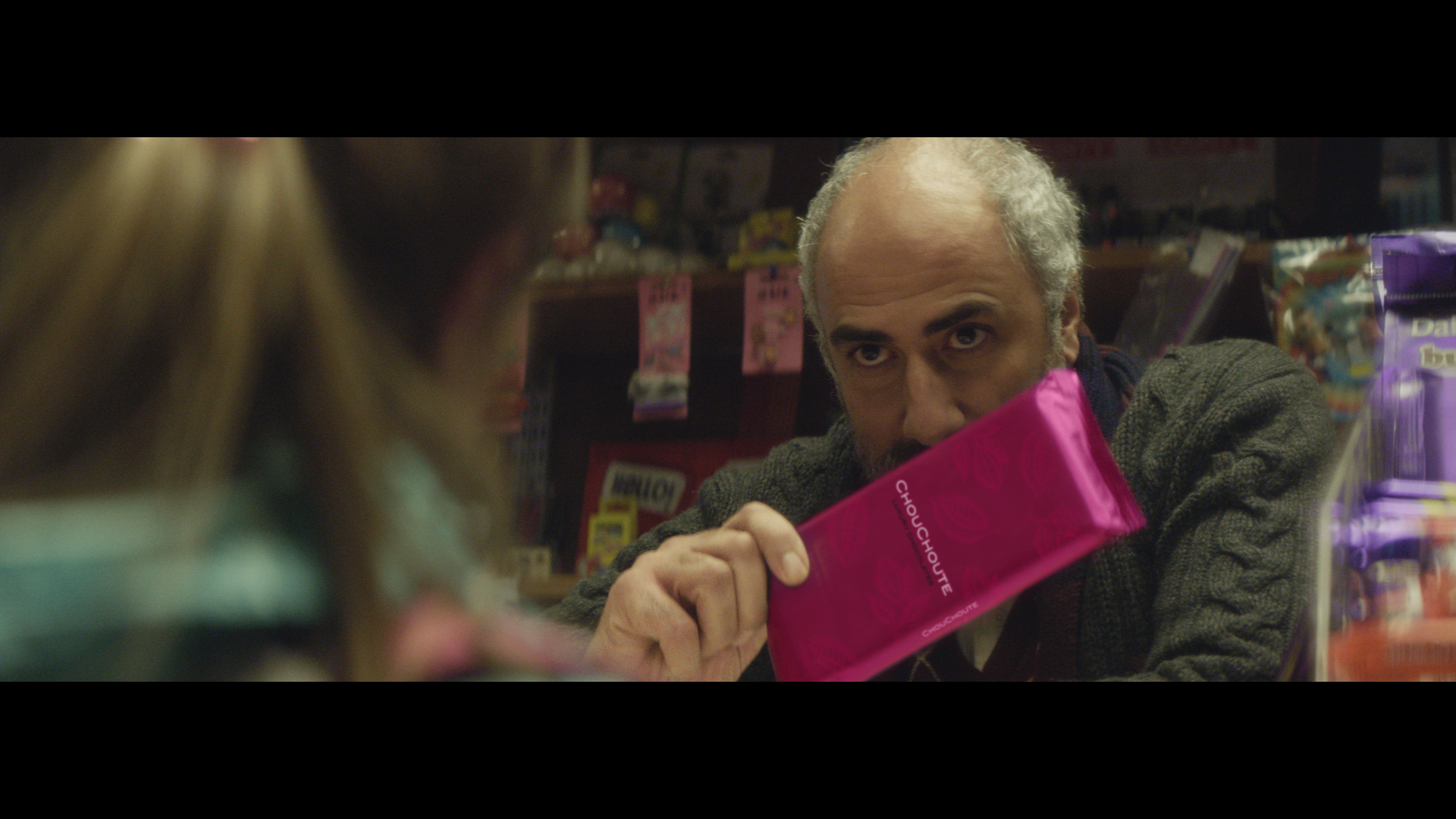 A shopkeeper holding a pink packaged chocolate bar