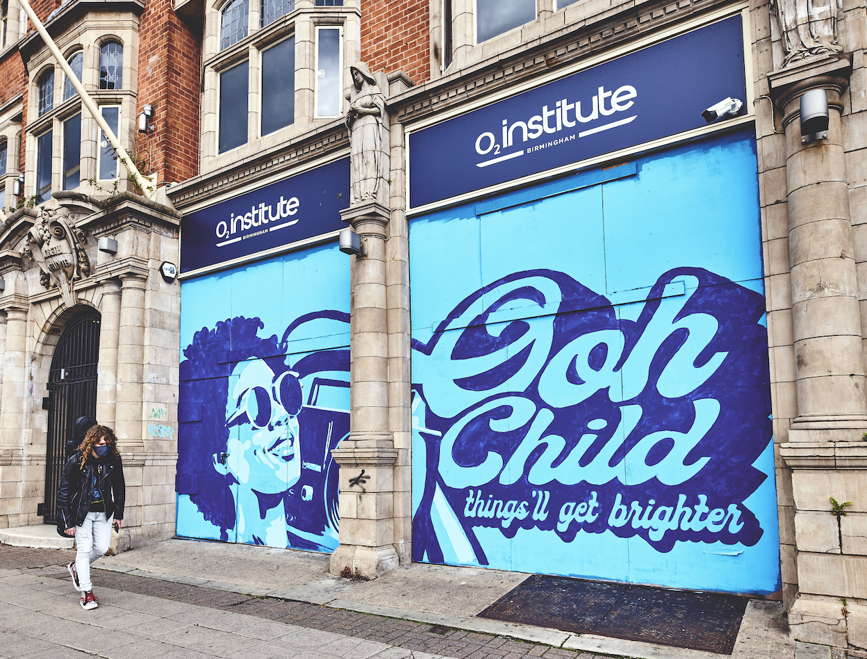 blue graffiti of a woman with sunglasses holding a boombox on a wall outside a music venue in Birmingham