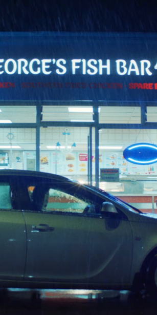An image of a car outside a fish restaurant. It's nighttime and raining.
