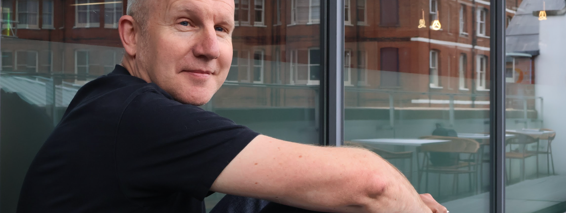 David Masterman sitting on a balcony at VCCP, looking relaxed and smiling at the camera.