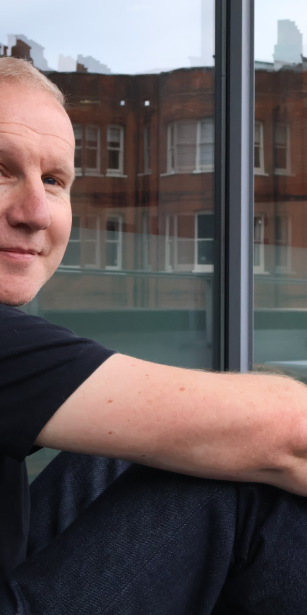 David Masterman sitting on a balcony at VCCP, looking relaxed and smiling at the camera.
