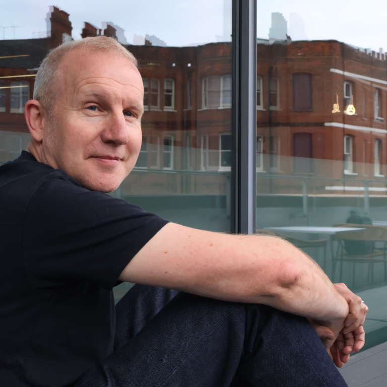 David Masterman sitting on a balcony at VCCP, looking relaxed and smiling at the camera.