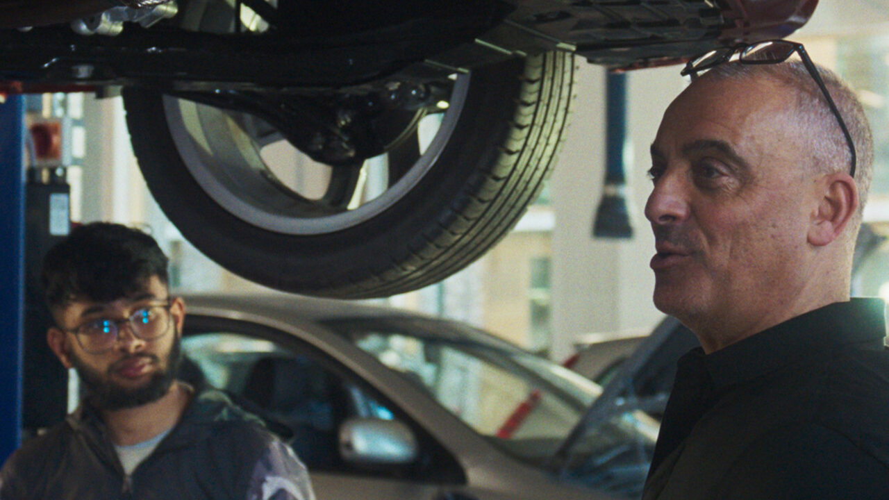 Department for Education campaign - Senior mechanic teaching a young person about fixing cars