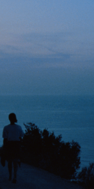 Two people on a coastal path at sunset illuminated by the light of a phone screen