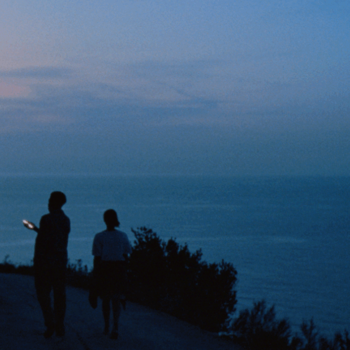 Two people on a coastal path at sunset illuminated by the light of a phone screen