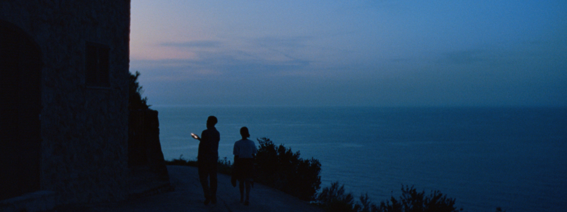 Two people on a coastal path at sunset illuminated by the light of a phone screen