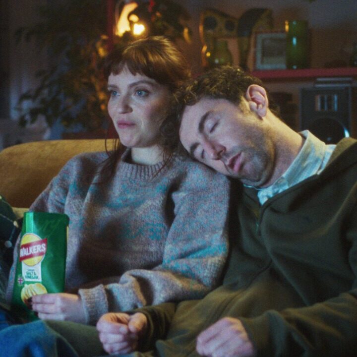 Woman watching TV on the couch eating Walkers crisps with someone laying on her shoulder. Walkers, VCCP