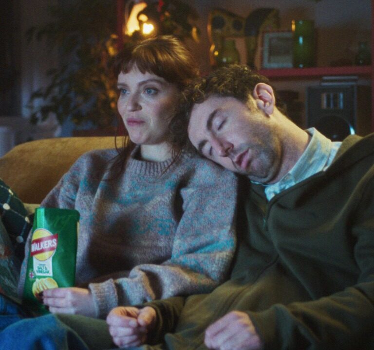 Woman watching TV on the couch eating Walkers crisps with someone laying on her shoulder. Walkers, VCCP