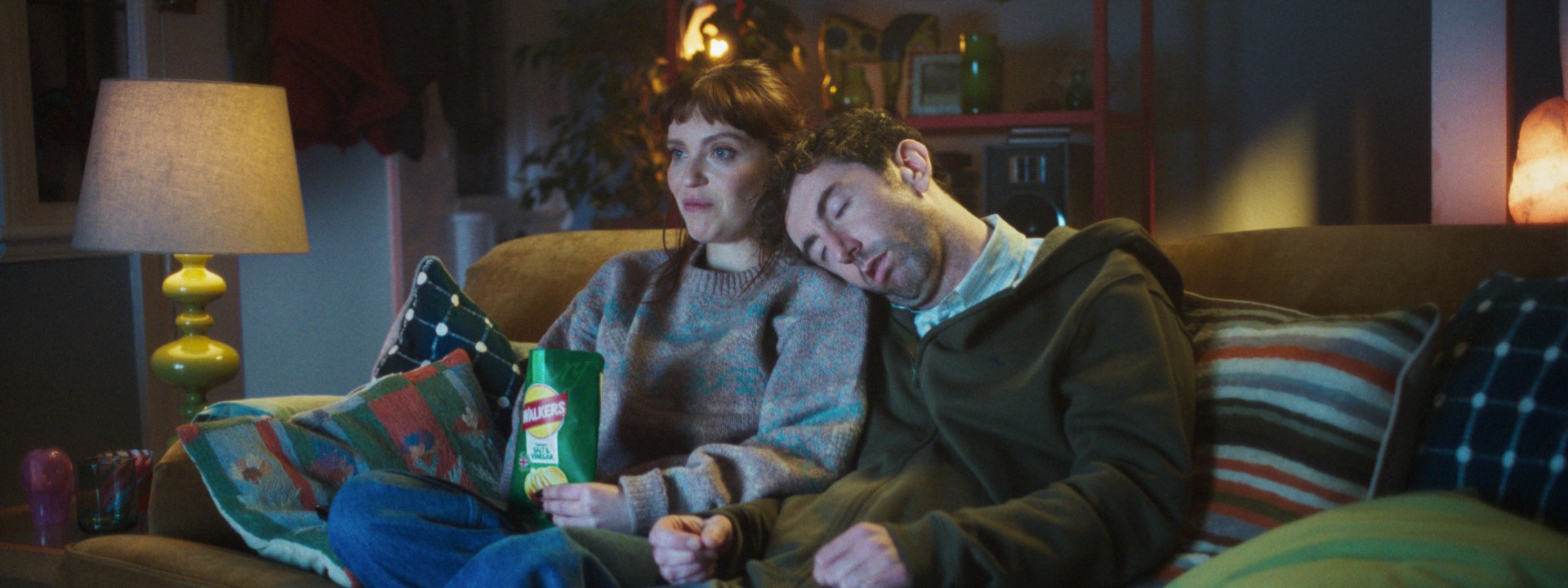 Woman watching TV on the couch eating Walkers crisps with someone laying on her shoulder. Walkers, VCCP