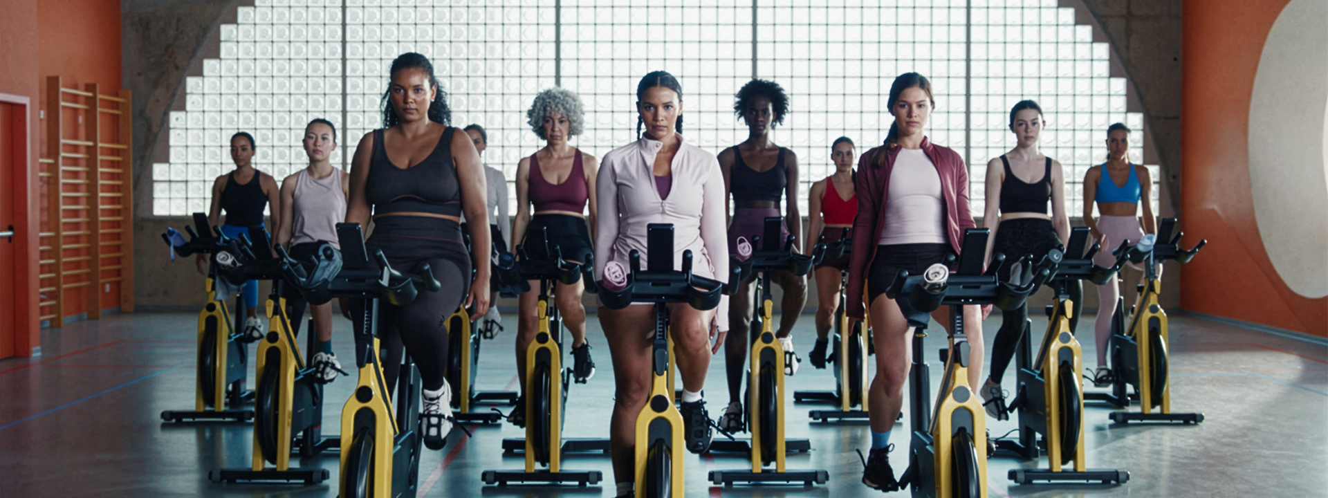 Diverse group of women riding stationary exercise bikes in a gym class wearing Primark activewear.