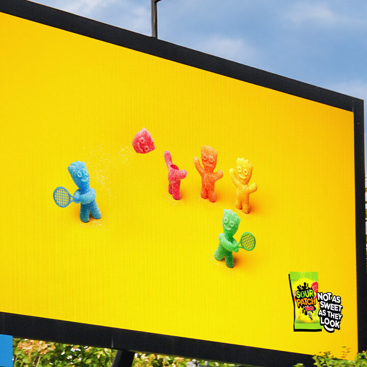 Digital billboard displaying Sour Patch Kids candy characters playing tennis using another sweet's head as a ball.