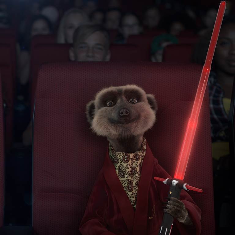 A meerkat wearing a red velvet jacket holding a light sabre in a cinema