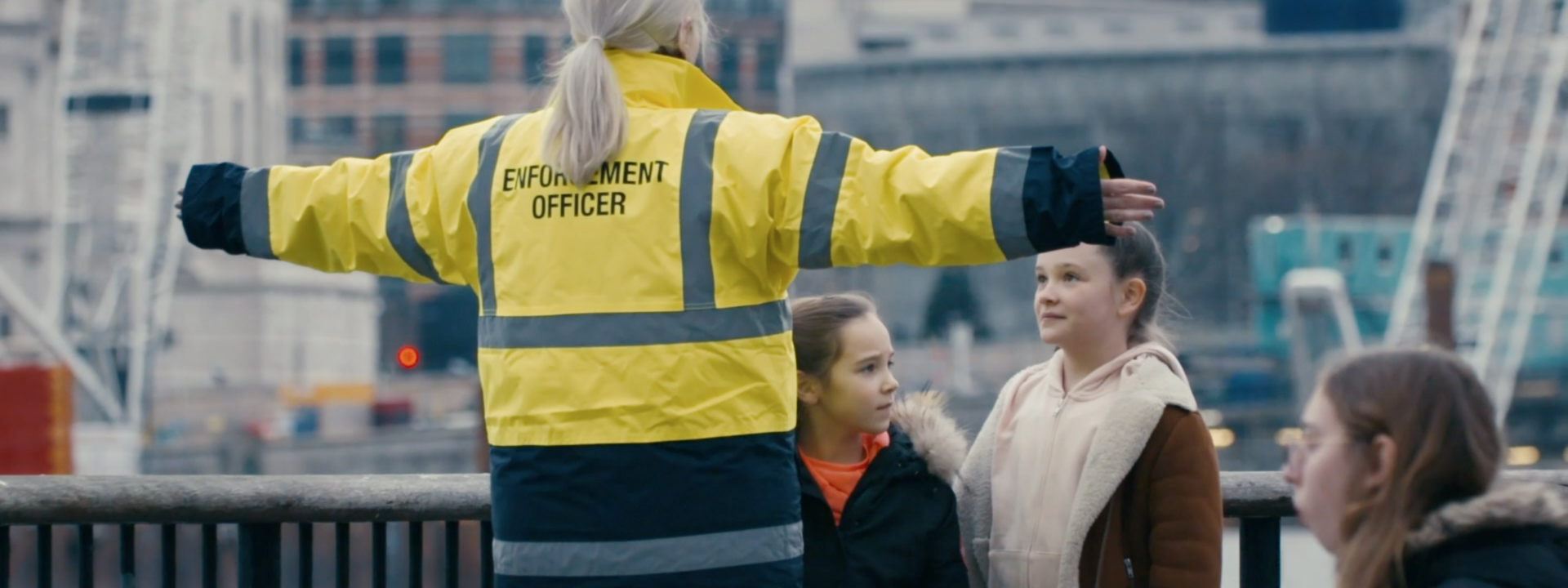 A woman in a high visibility jacket with their arms stretched out to block people from getting passed her