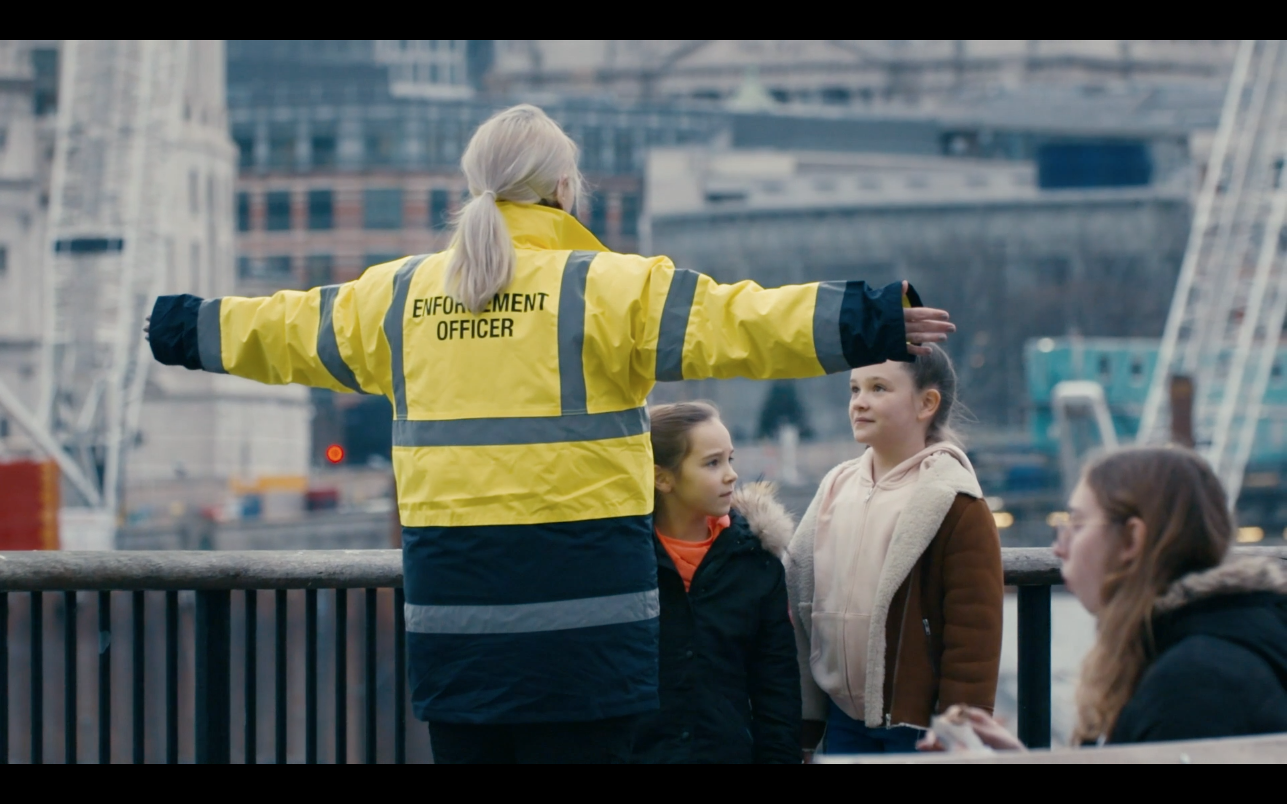 A woman in a high visibility jacket with their arms stretched out to block people from getting passed her