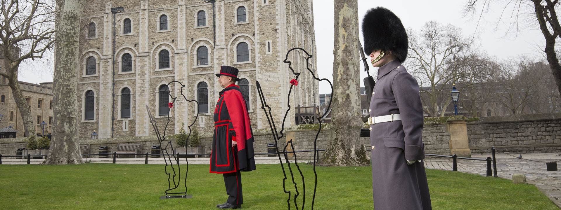 Two men in uniform alongside an iron silhouette of a soldier wearing a poppy on their chest