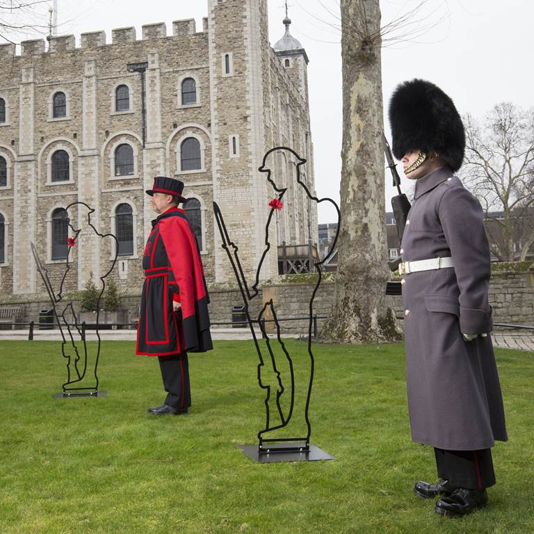 Two men in uniform alongside an iron silhouette of a soldier wearing a poppy on their chest