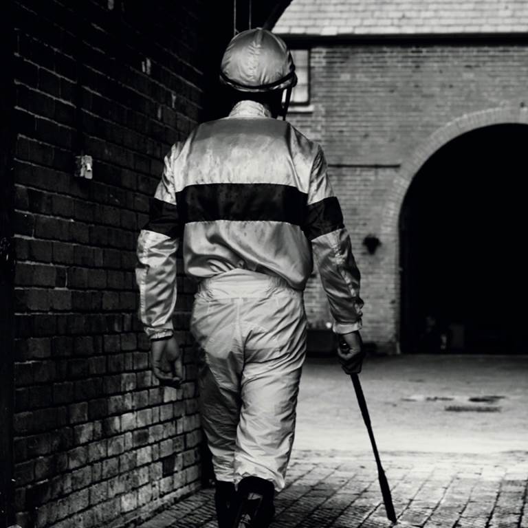 A horse riding jockey from behind holding a crop