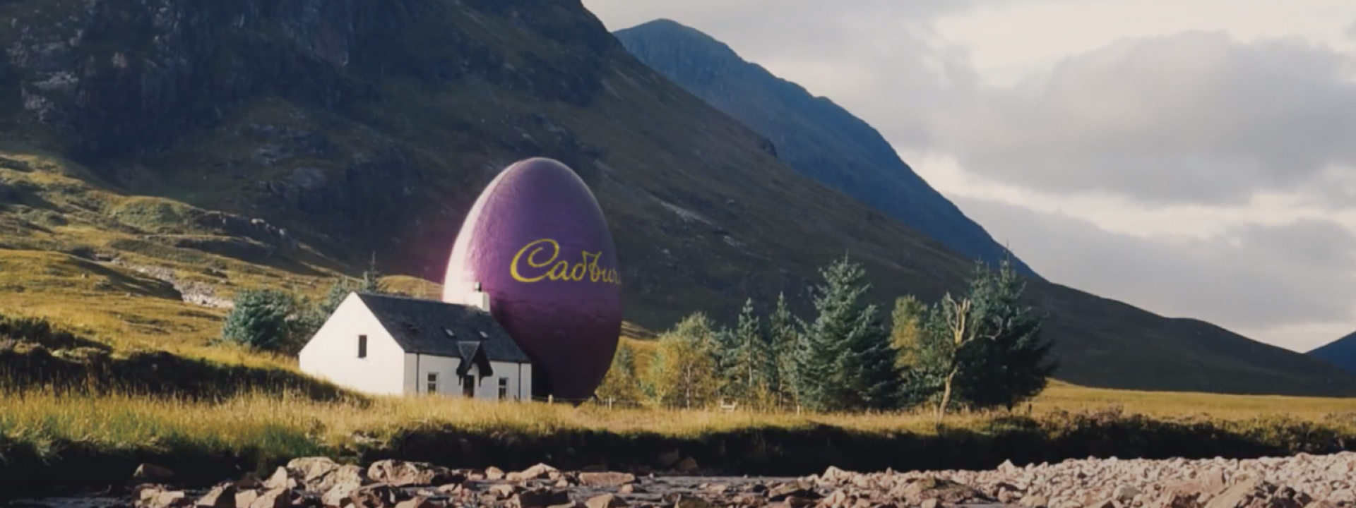 Countryside landscape scene with a giant purple Cadbury branded egg placed next to a house