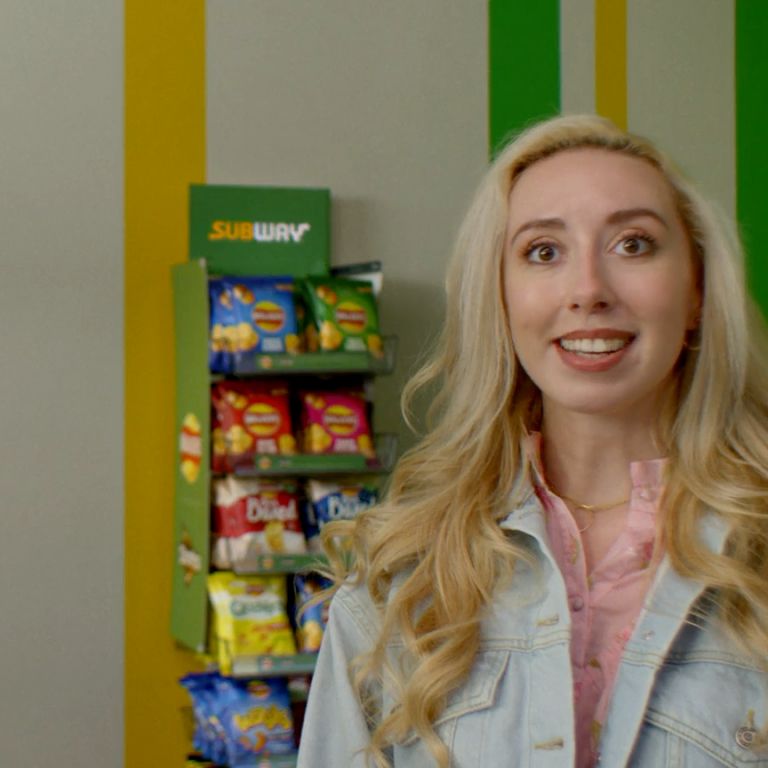 A couple in a Subway fast food restaurant with the Walkers crisps range displayed on a shelf behind them