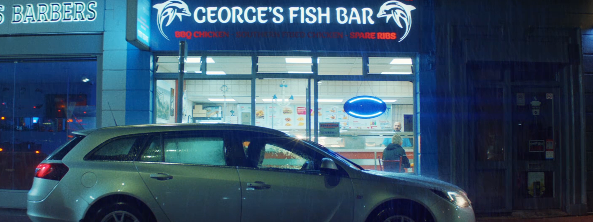 An image of a car outside a fish restaurant. It's nighttime and raining.