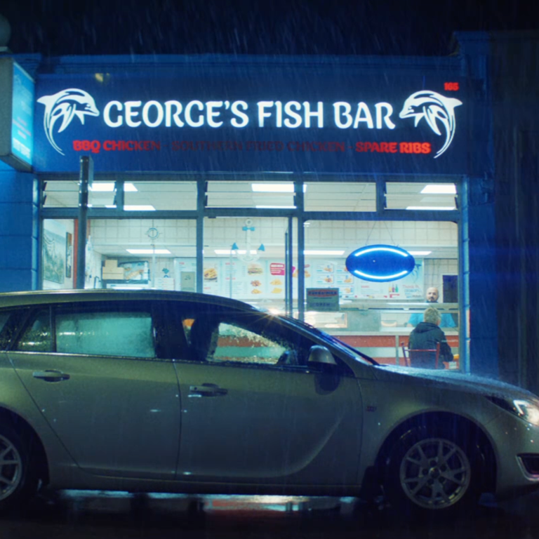 An image of a car outside a fish restaurant. It's nighttime and raining.