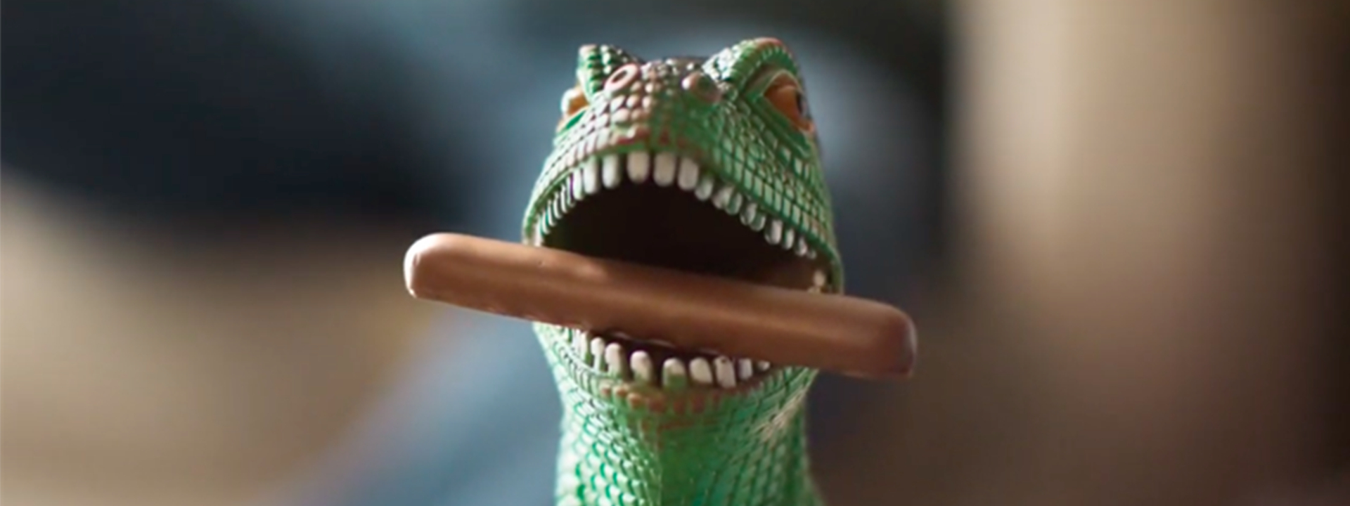 A toy dinosaur with a Cadbury Dairy Milk Finger biscuit in its mouth