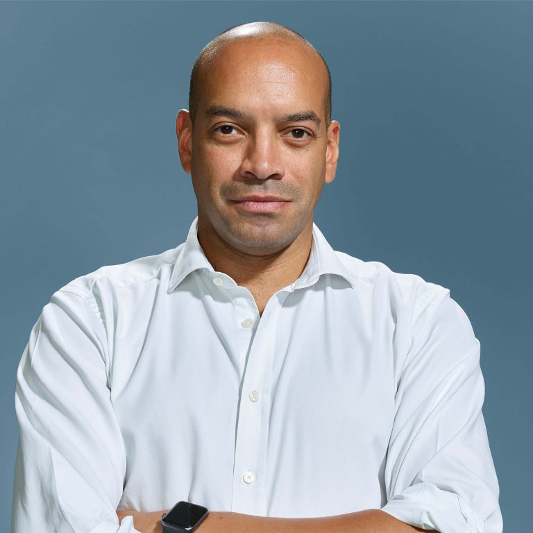 Headshot image where Dougie looks face-on at the camera, he is wearing a white shirt and has his arms crossed.