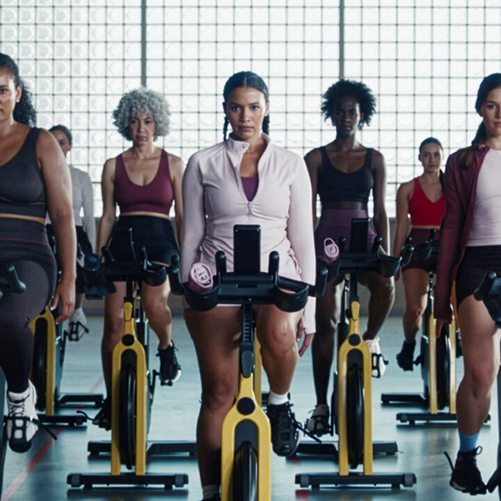 Diverse group of women riding stationary exercise bikes in a gym class wearing Primark activewear.