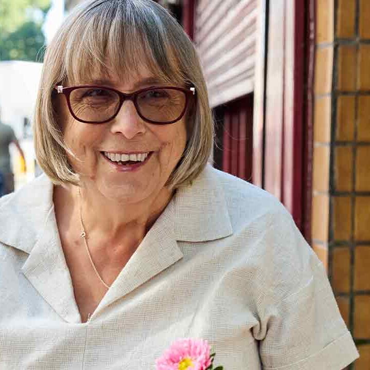 Happy senior woman with bob haircut and glasses smiling while interacting with a friend outside a shop.